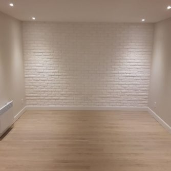 Grande pièce avec plancher de bois et mur de briques blanches rénové par Rénovation Simtech
